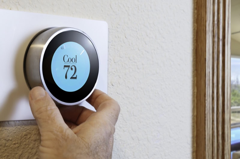 10 Tips to Get the Most Benefits From Your Smart Thermostat. Photo of someone adjusting a digital thermostat mounted on a wall.